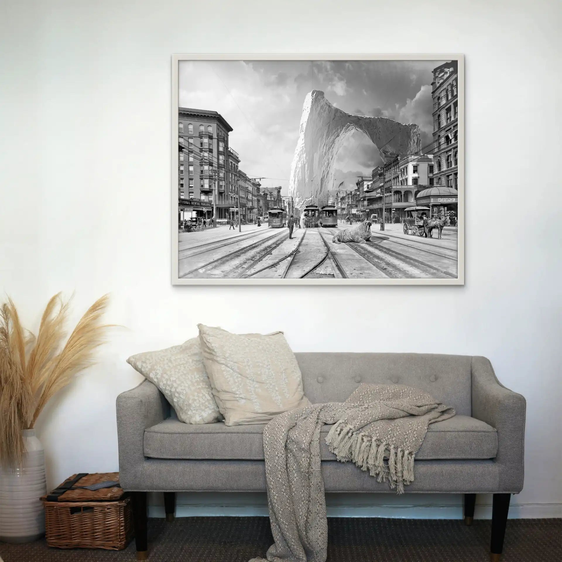 Tableau noir et blanc montrant des tramways devant un iceberg géant, accroché au-dessus d'un canapé gris avec coussins.