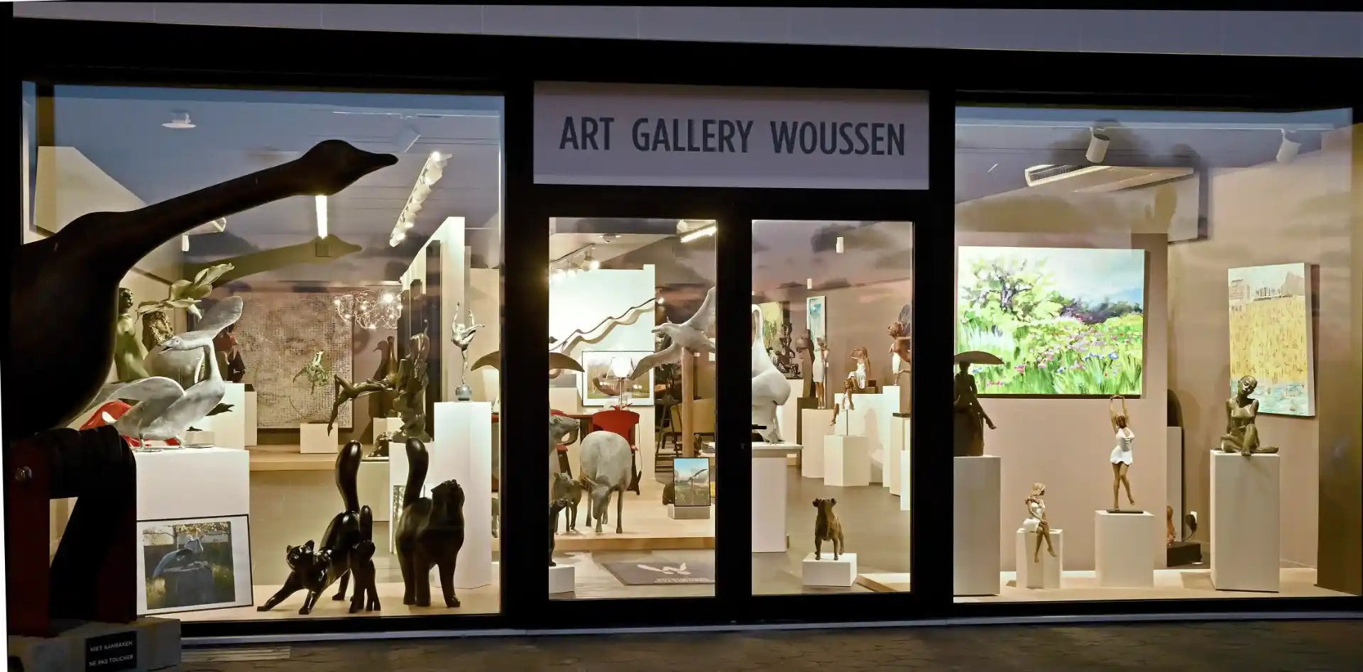Vitrine de la galerie d'art Woussen artkornergallery présentant diverses sculptures d'animaux et de figures humaines, ainsi que des peintures exposées à l'intérieur.